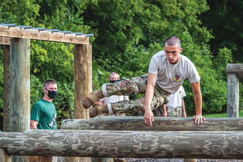 A cadet jumps over the low hurdles on the obstacle course while other cadets watch.