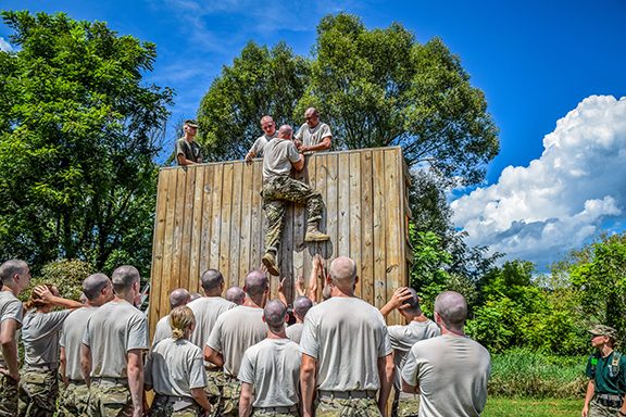 Cadets pull another cadet up a large wooden wall.