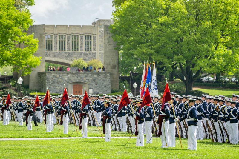 The cadet regiment stands on the Drillfield in dress uniforms. The Pylons and War Memorial Chapel are in the background.