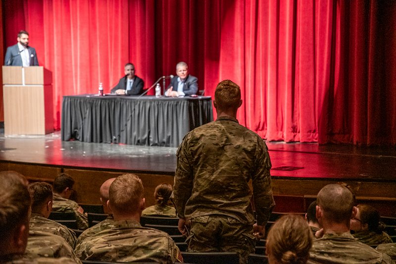 A cadet asks a question during a panel discussion with two businessmen.